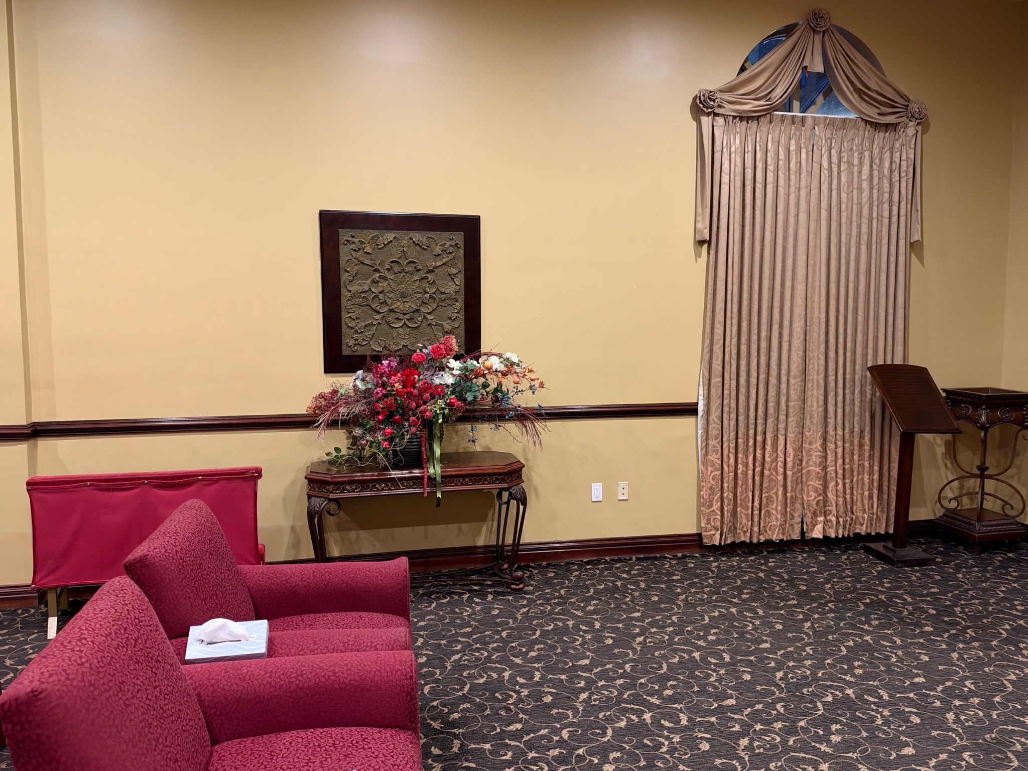 Upholstered seating beside a floral arrangement and draped chapel window.